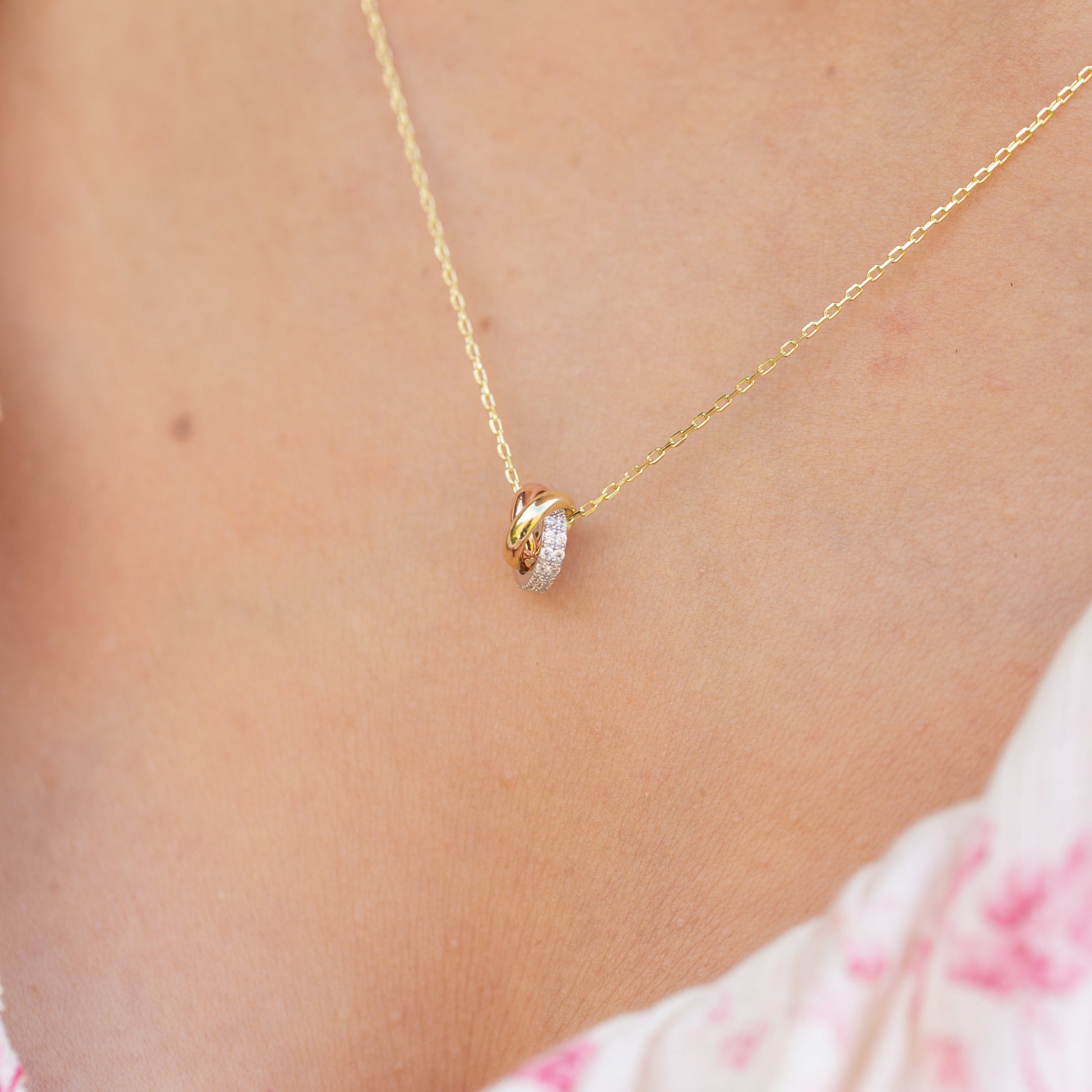 Gold necklace with a heart pendant worn by a person in a floral outfit