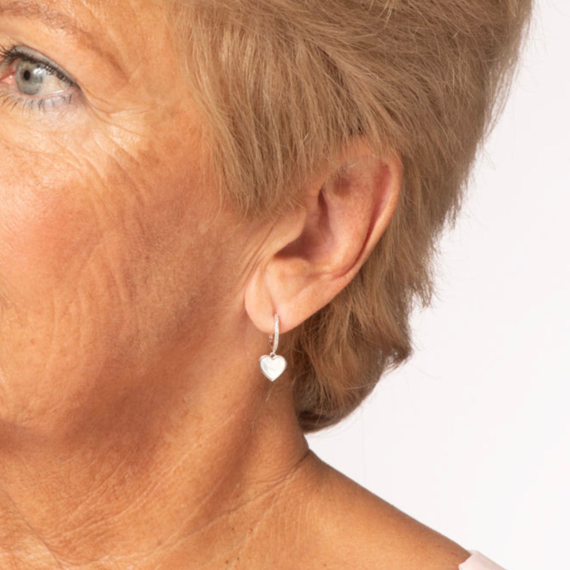 Close-up of a person wearing a heart-shaped earring on a white background