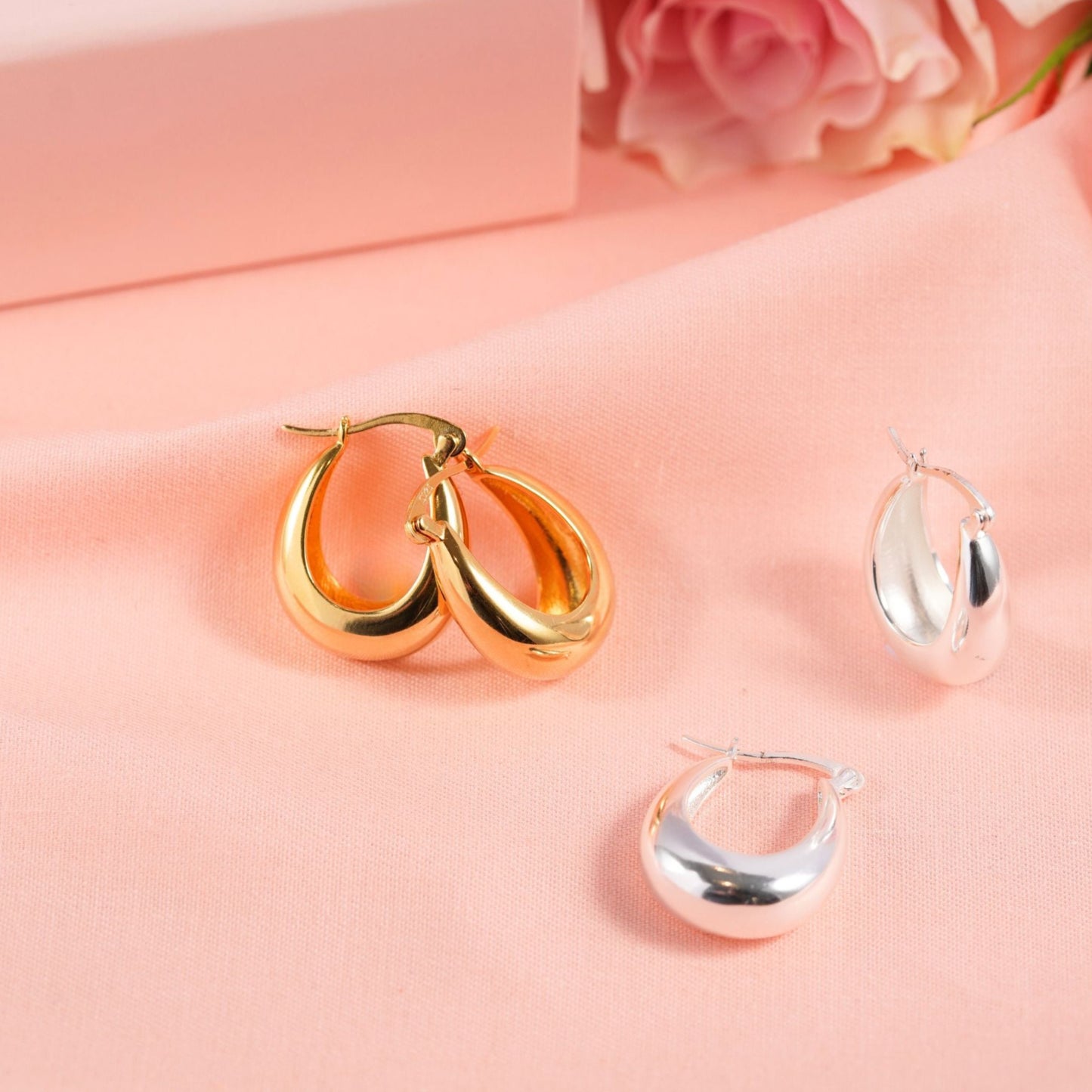 Gold and silver hoop earrings on a pink surface with pink roses.