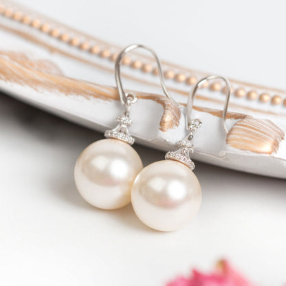 Pearl hook earrings with round white pearls and jeweled caps laid on a box