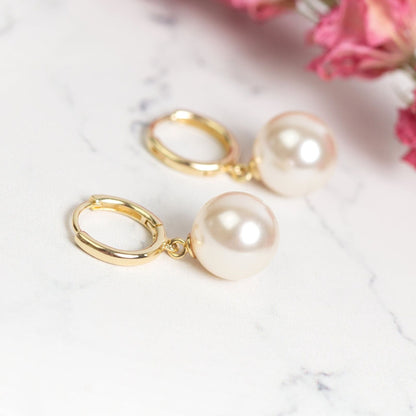Gold huggie hoop earrings with large white pearl drops on jewelry surface