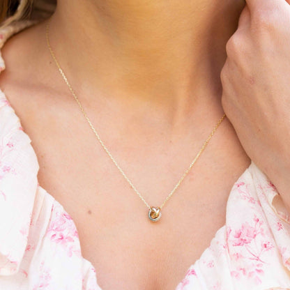 Gold knot necklace pendant at neckline with small sparkle detail