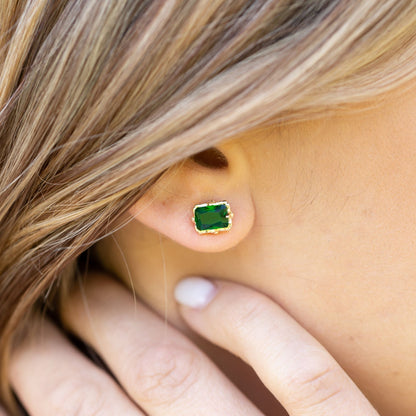 Gold emerald stud earring with square green gemstone and ornate bezel, on ear