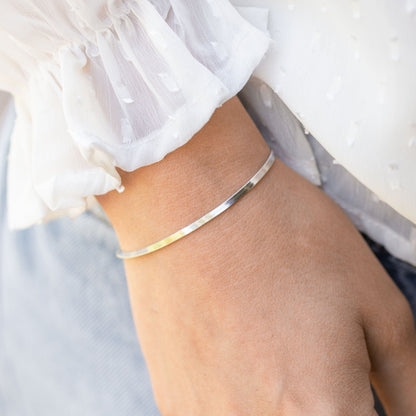 Silver flat snake chain bracelet on wrist, slim curved band