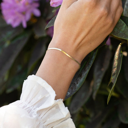 Gold flat snake chain bracelet on wrist with slim curved silhouette