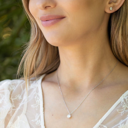 Moissanite diamond pendant on silver chain worn at neckline, round prong-set stone