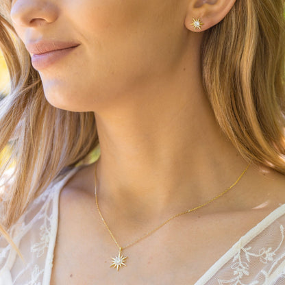 Gold starburst pendant necklace with crystal sunburst charm resting on chest