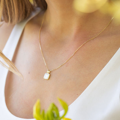 Pendant necklace with square mother-of-pearl charm on gold chain worn on neckline