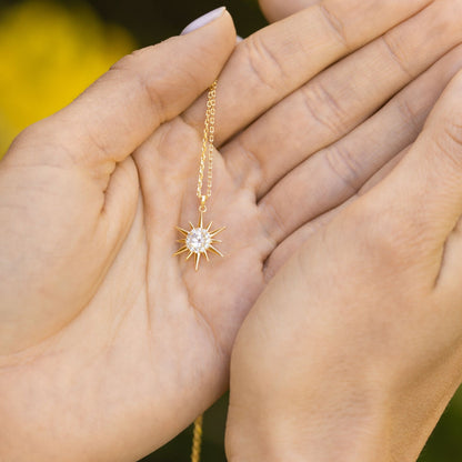 Gold starburst pendant necklace chain held in hand with crystal sunburst charm